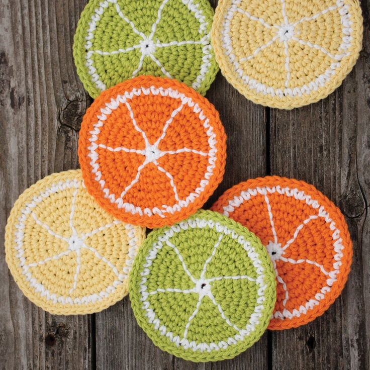 crocheted citrus coasters are arranged on a wooden surface, ready to be used as placemats