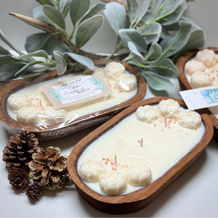 three wooden trays filled with soap and pine cones on top of a white table