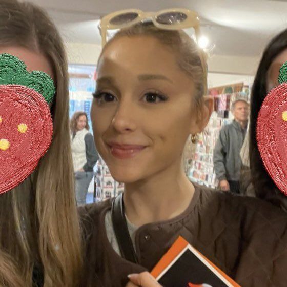 two women with fake strawberrys on their faces and one woman holding a book in front of her face