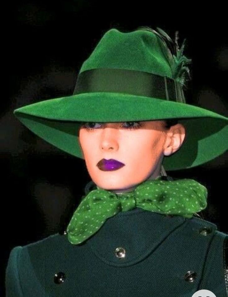 a woman wearing a green hat with a bow tie on her neck and dark background