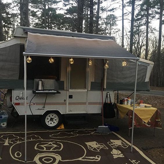 an rv is parked in the woods with its awning open and it's lights on