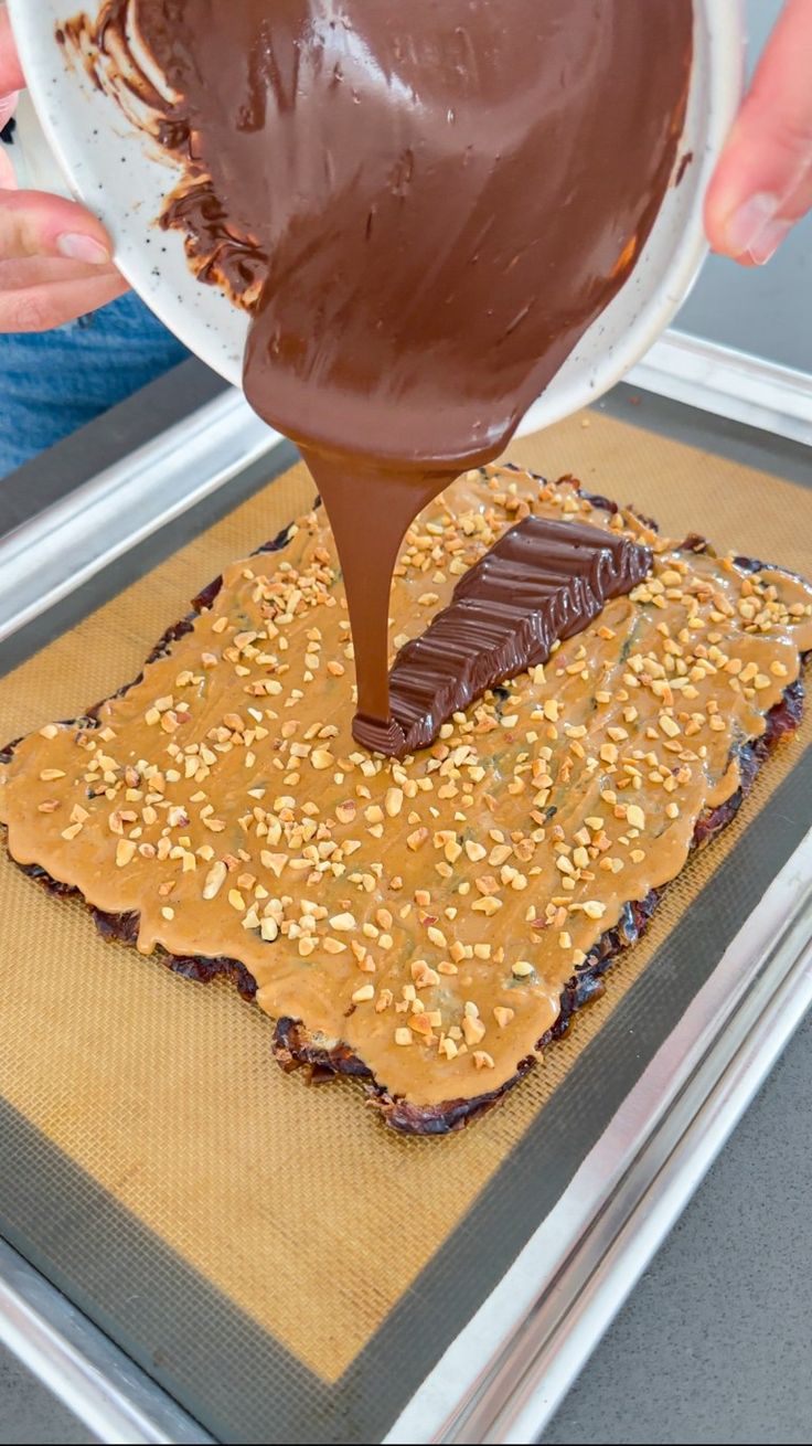 someone is spreading chocolate on top of peanut butter crackers and peanuts to make an appetizer