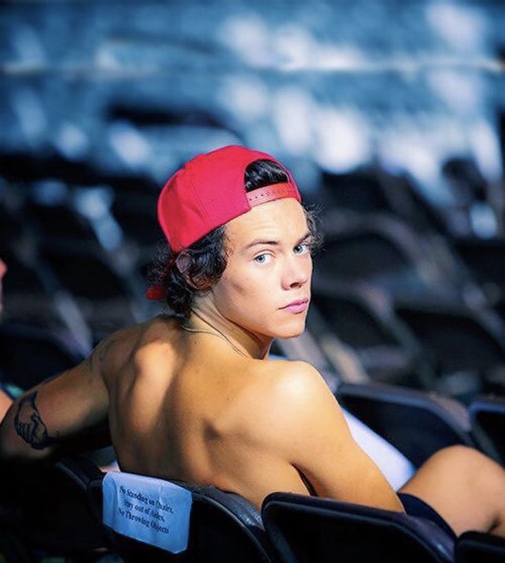 a shirtless man wearing a red hat sitting in an auditorium with other people behind him