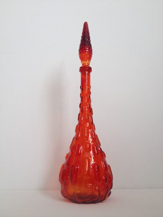 an orange glass vase with a small red cone on it's top, sitting in front of a white wall