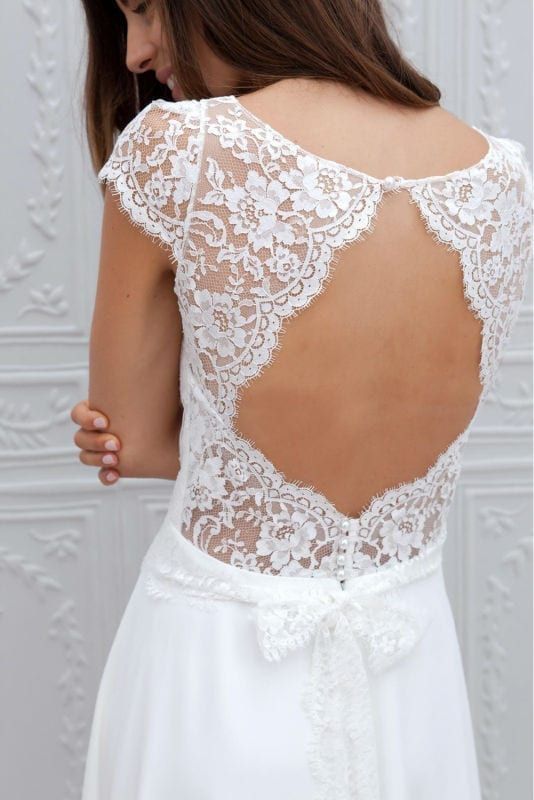 the back of a woman's wedding dress with white lace and bows on it