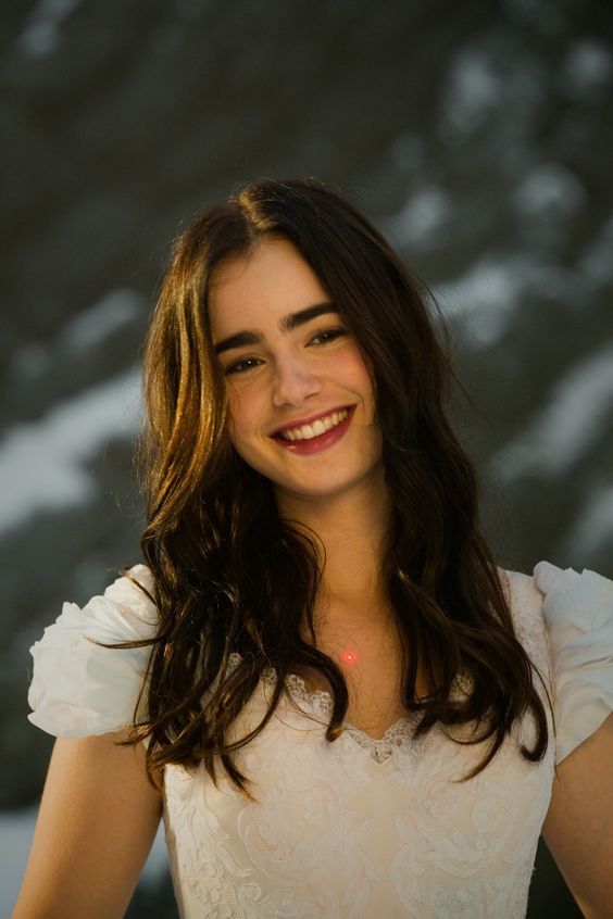 a woman with long hair smiling and wearing a white shirt in front of a snow covered background