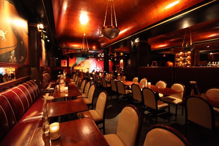 a dimly lit restaurant with wooden tables and white upholstered chairs in front of the bar