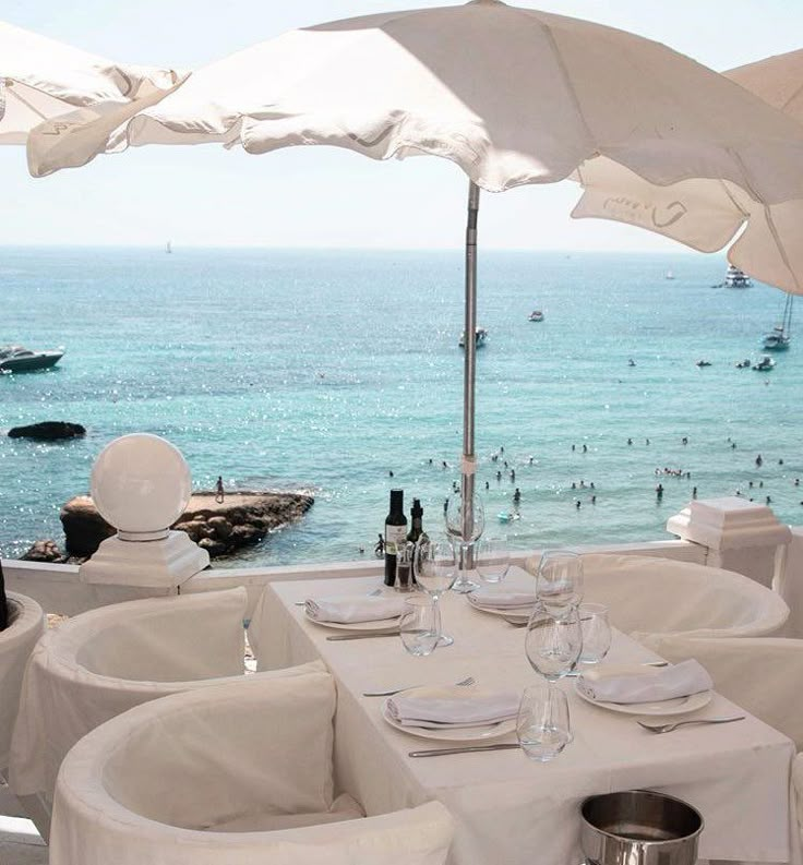 an outdoor dining area overlooking the ocean with umbrellas and tables set up for two