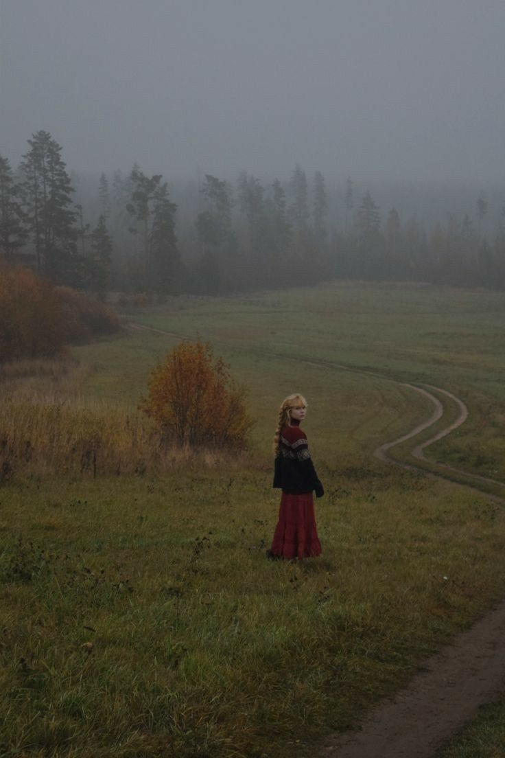 a woman standing on top of a lush green field next to a forest filled with trees