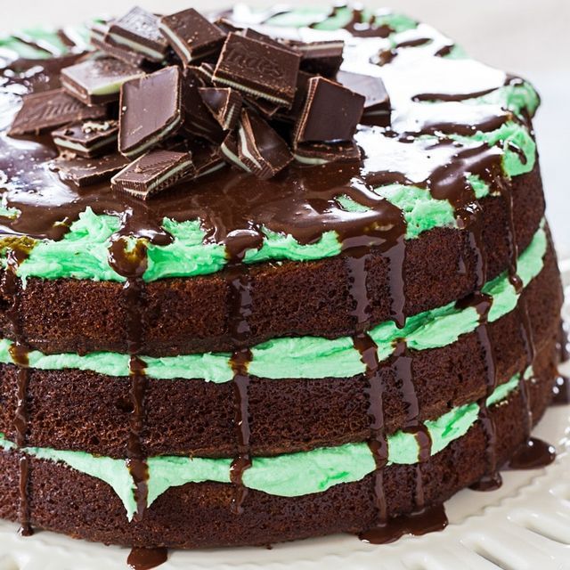 a chocolate cake with green frosting and chocolate chips on top, sitting on a white plate