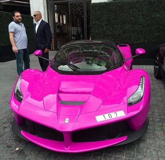 two men standing next to a pink sports car