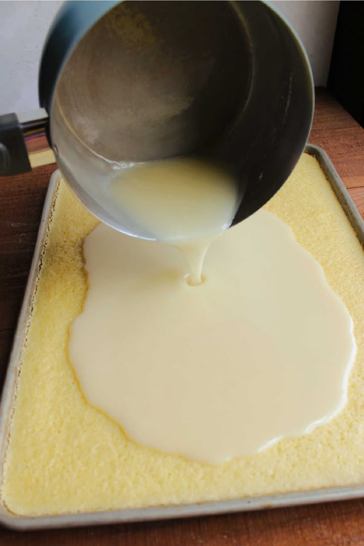 a person pouring white sauce on top of a pan