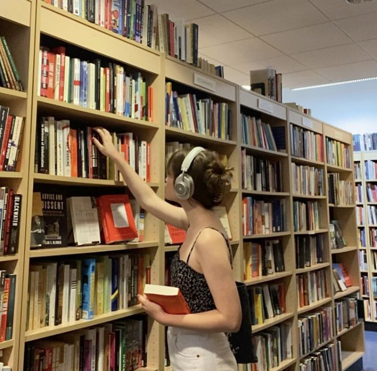 a woman standing in front of a bookshelf with headphones on