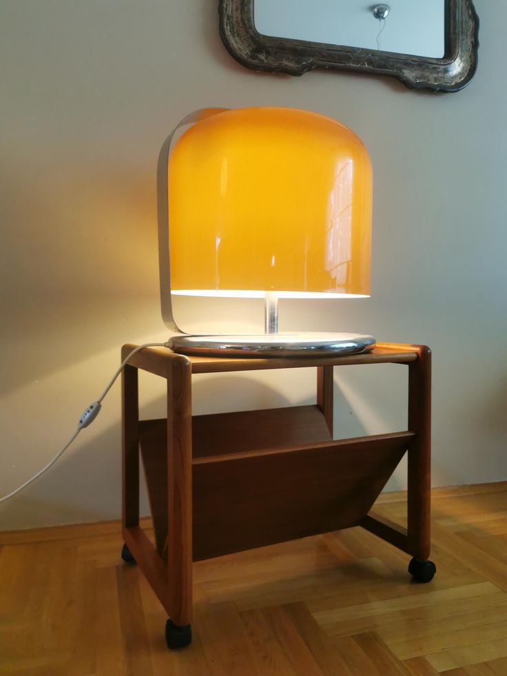 a yellow lamp sitting on top of a wooden table next to a mirror and wall