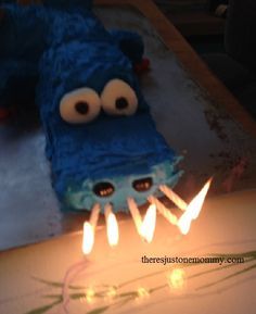 a birthday cake that looks like a blue monster laying on the ground with candles in front of it