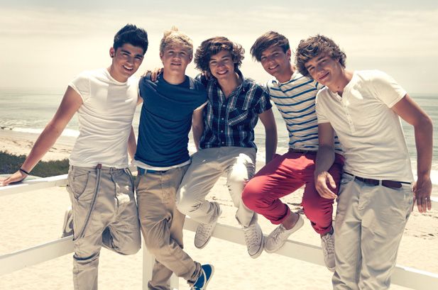 four young men are posing for a photo on the boardwalk near the beach, with an ocean in the background