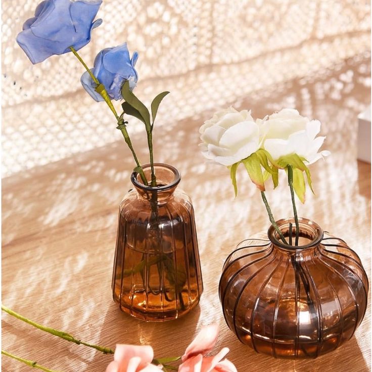 two vases with flowers in them sitting on a wooden table next to each other