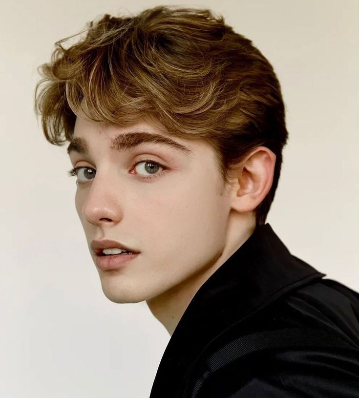 a young man with brown hair and blue eyes looks at the camera while wearing a black shirt