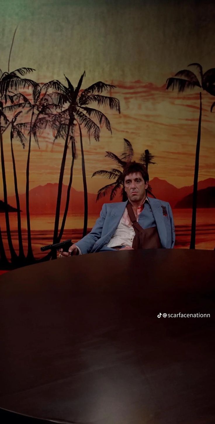 a man sitting at a desk in front of a painting with palm trees on it