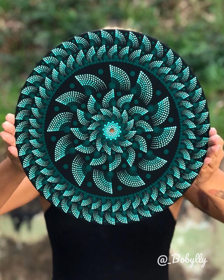 a woman holding up a green and black plate with an intricate design on the front