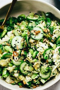 a white bowl filled with cucumber and other vegetables next to a wooden spoon