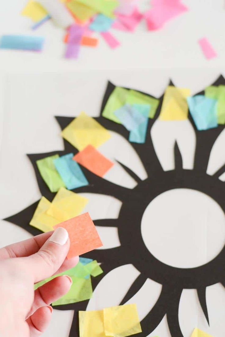 someone is making a paper flower with colored sticky notes on the side and one hand pointing at it