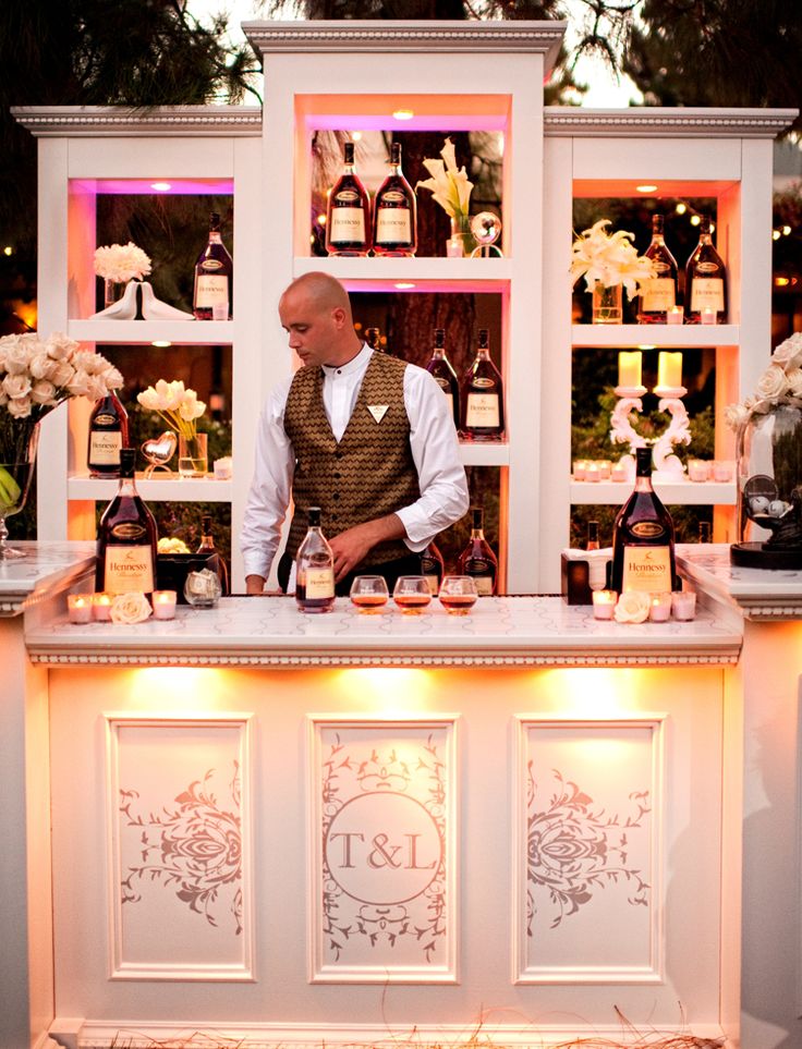 a man standing behind a bar filled with liquor bottles and candles on top of it