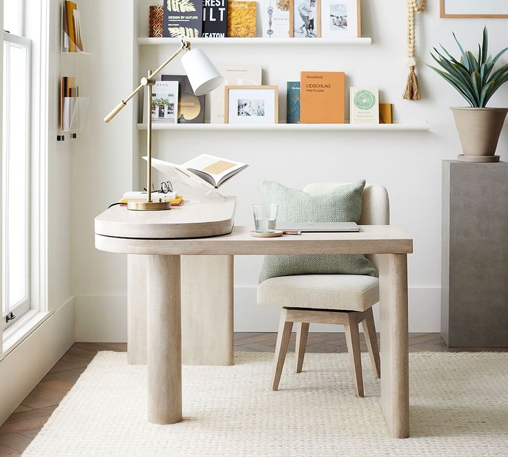 a desk with a chair, lamp and pictures on the wall above it in a white room