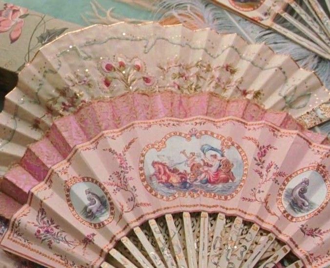 an ornately decorated hand fan is seen in this image, with pink and gold accents