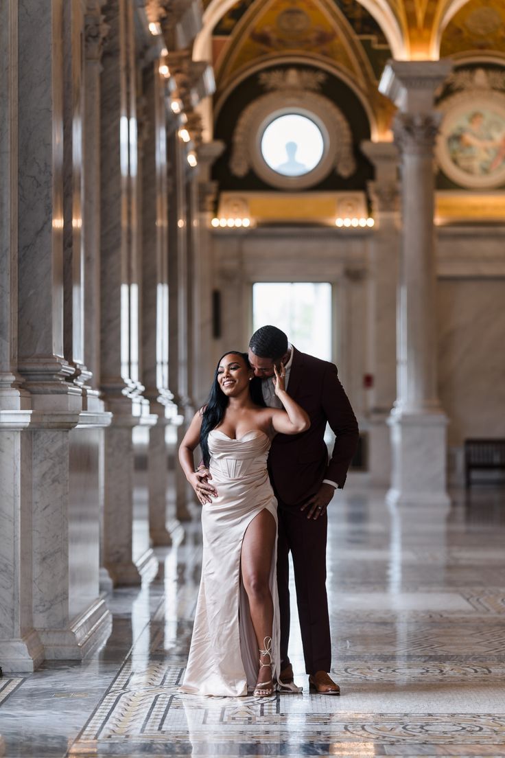 a man and woman posing for a photo in an ornate building with columns on either side