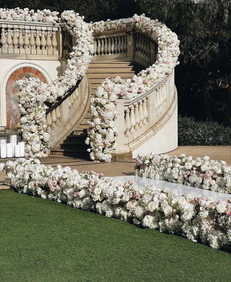 an outdoor wedding setup with white flowers and candles on the grass next to stairs in front of a building