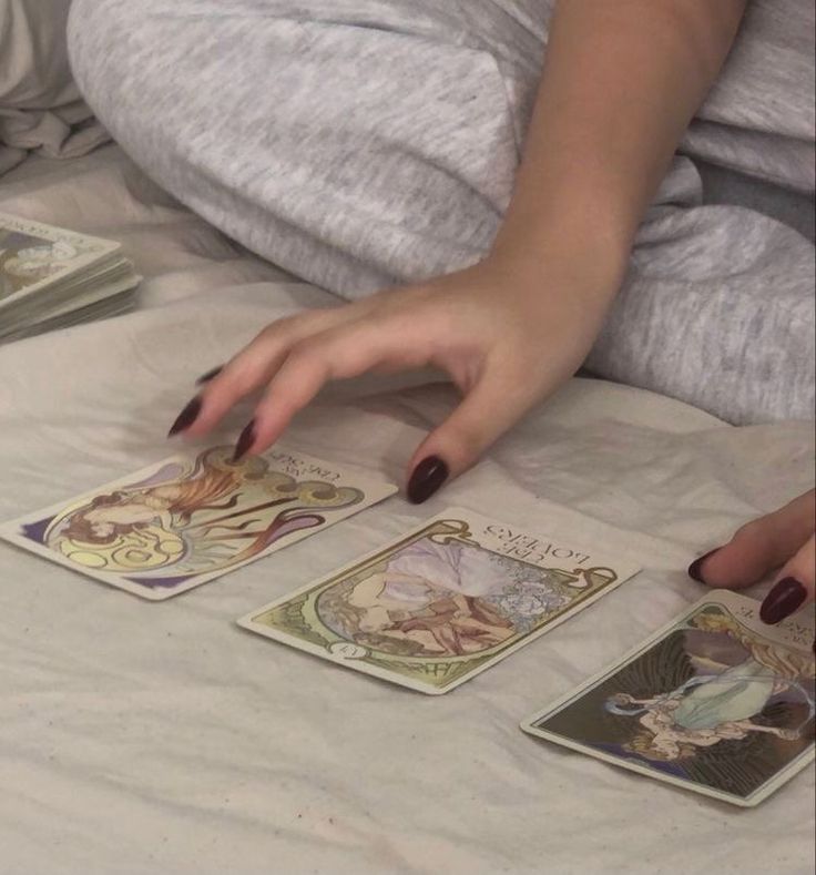 a woman laying in bed with four tarot cards on top of her stomach and one hand reaching for the tarot card