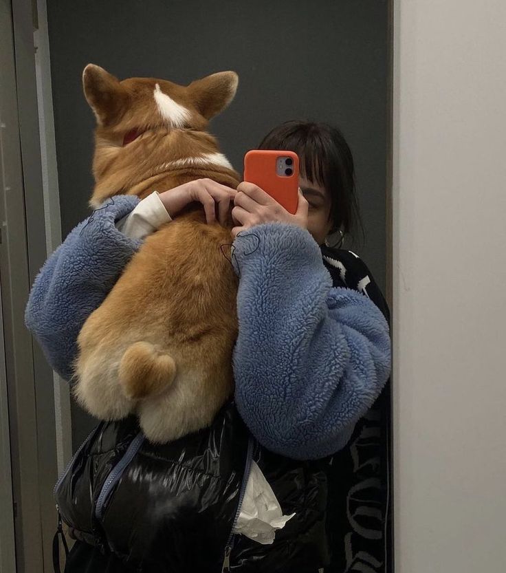 a woman taking a selfie with her phone while holding a corgi dog