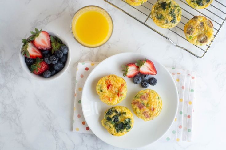 some muffins and fruit on a plate next to a glass of orange juice