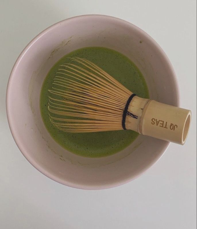 a whisk in a white bowl filled with green liquid