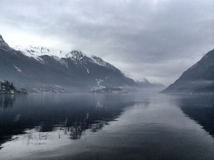 a body of water surrounded by mountains and snow covered peaks in the distance, with houses on either side