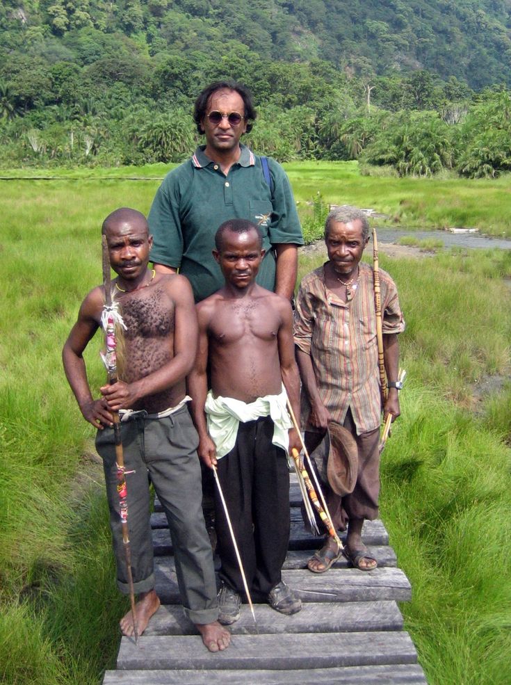 a group of men standing on top of a wooden platform in the grass with trees in the background