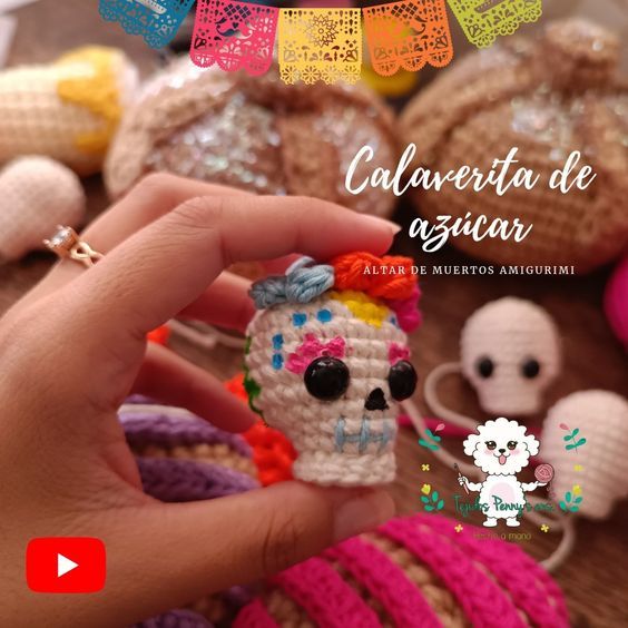 a hand holding a small crocheted sugar skull in front of other skulls and toys