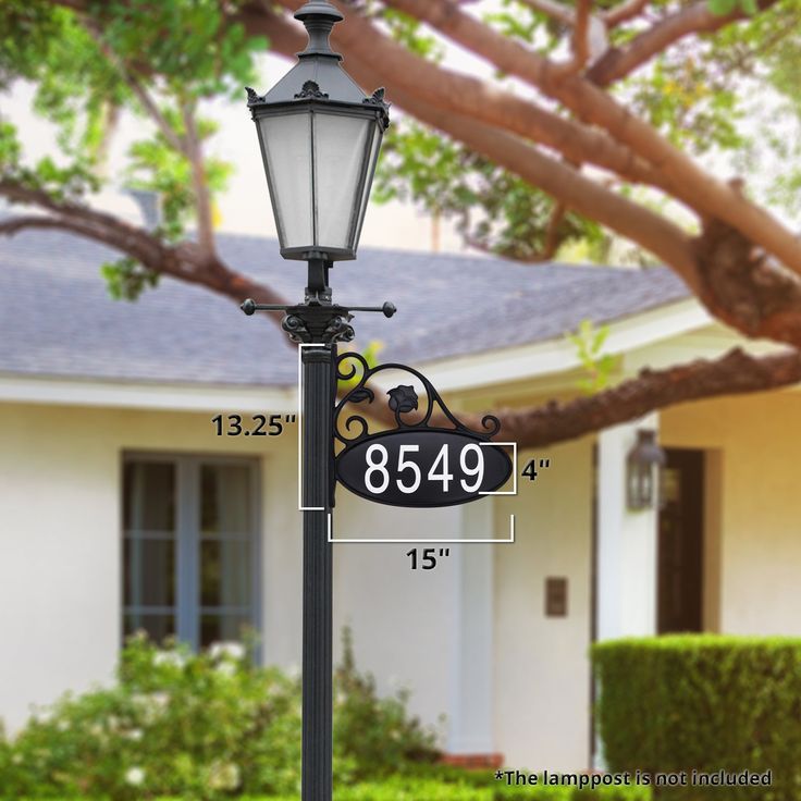 a lamp post with a address sign on it in front of a house and tree