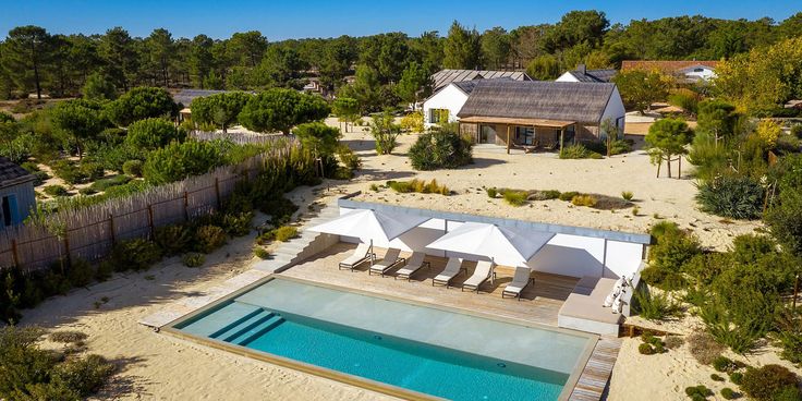 an aerial view of a house with a swimming pool in the foreground and trees surrounding it