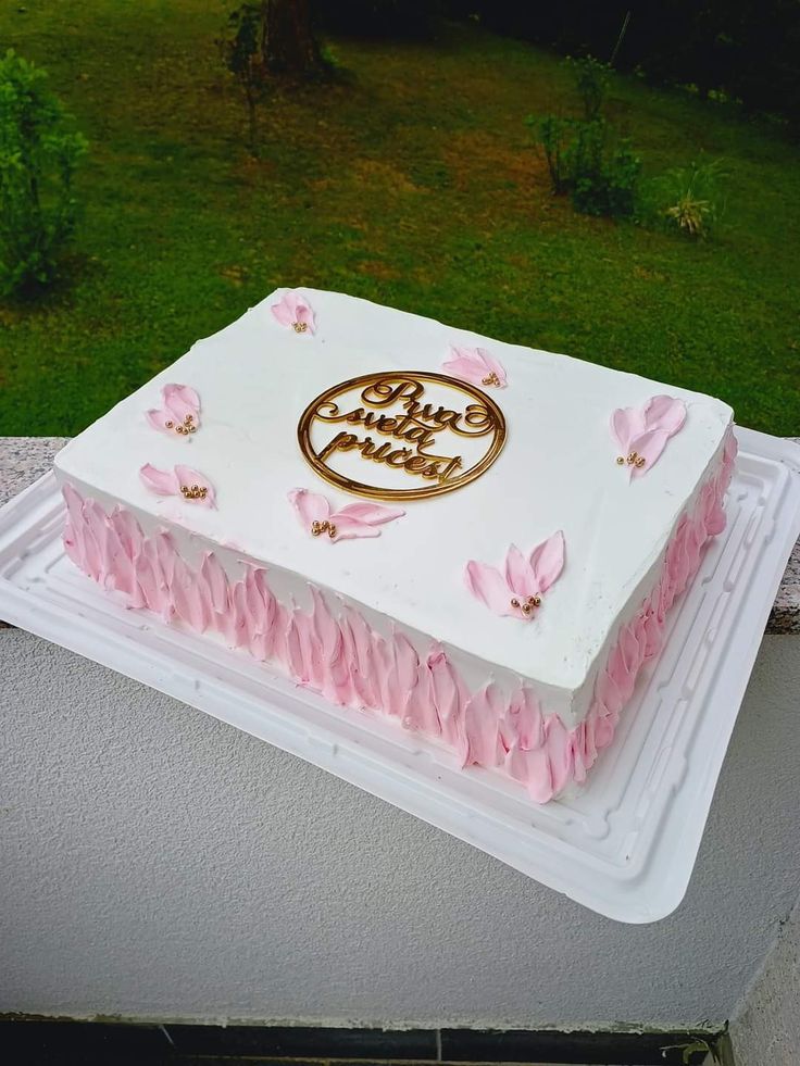 a white and pink cake on top of a plastic tray in front of a green lawn