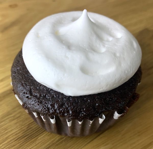 a chocolate cupcake with white frosting on a wooden table, ready to be eaten