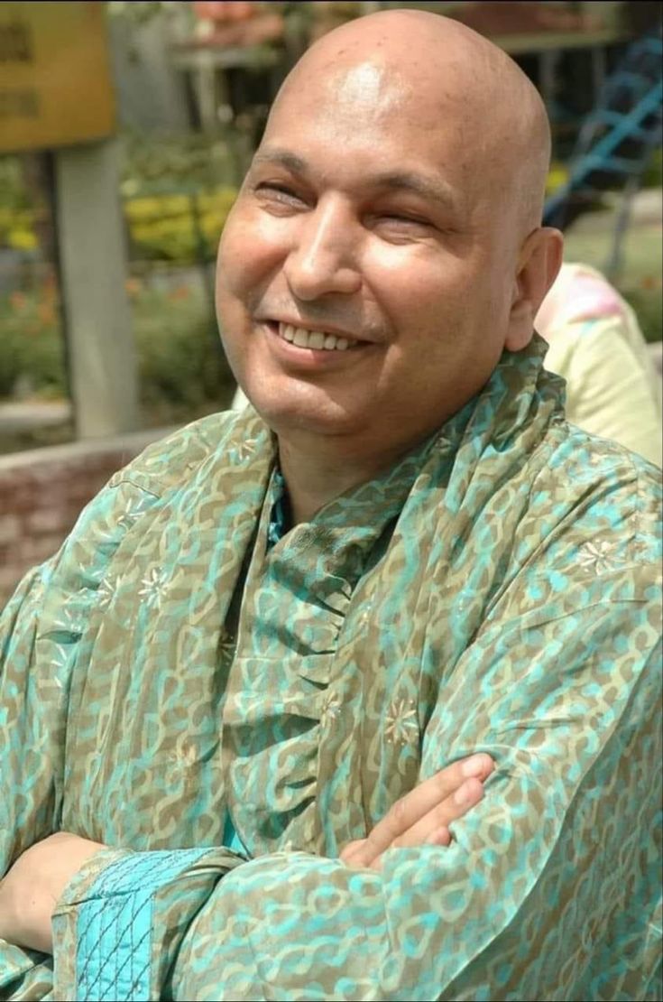 a bald man with his arms crossed smiling at the camera while wearing a green shirt