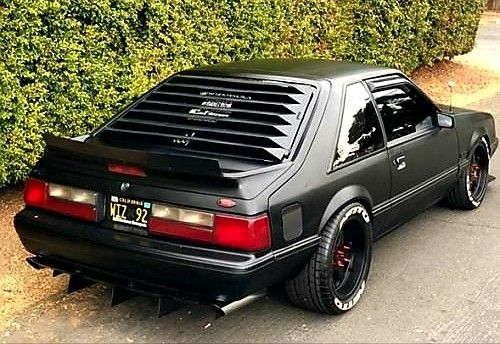 a black car parked in front of a hedge