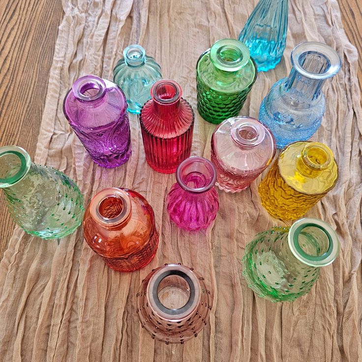 there are many different colored glass vases on the table together and one is empty