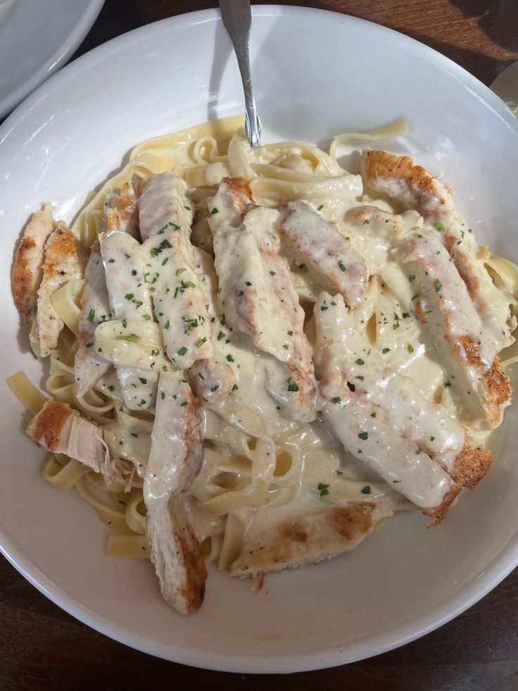 a white plate topped with pasta and chicken covered in gravy on top of a wooden table