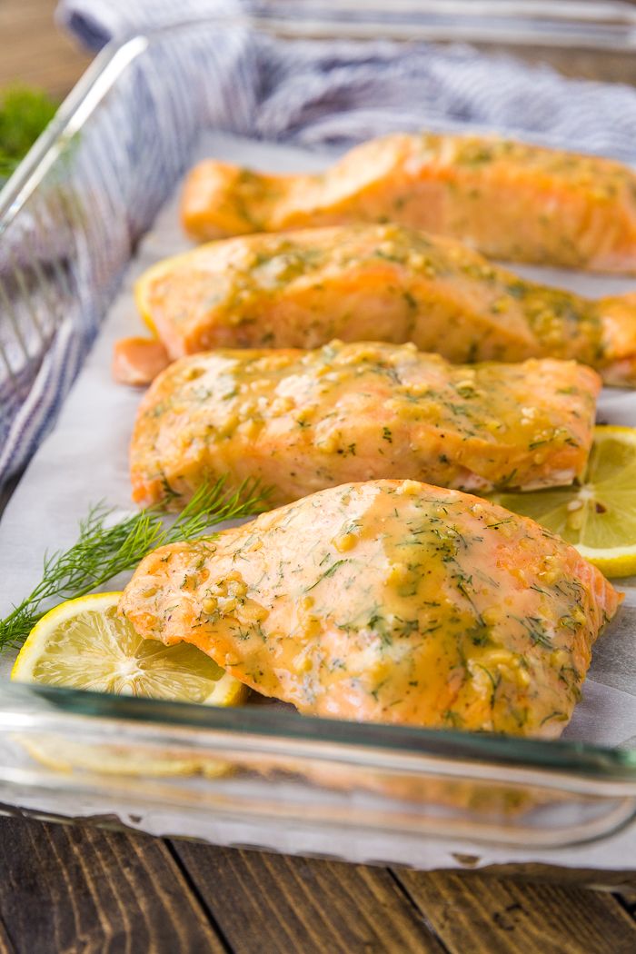 salmon fillets in a glass dish with lemon wedges and dill on the side