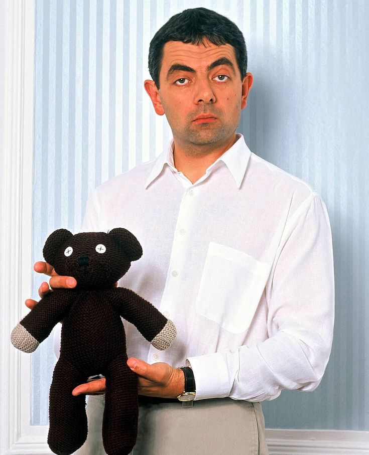 a man holding a teddy bear in front of his face while standing against a wall