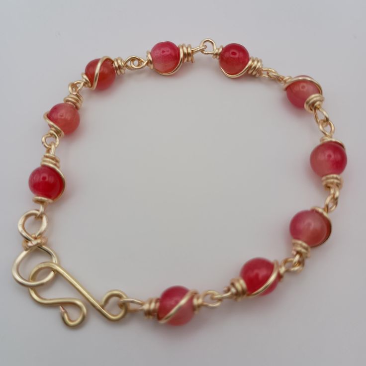 These bracelets feature a combination of brilliant red beads, wrapped in gold wire. The beads are evenly spaced and secured with a decorative wire-wrapping technique. The closure is a handmade hook clasp, also in gold enamel copper based wire, which adds a unique handmade touch. The beads are wrapped in gold enamel copper base wire in a consistent style, giving it a cohesive and elegant look. Adjustable 14k Gold-filled Bracelet With Beads, Adjustable Gold-tone Metal Beaded Bracelet, Adjustable 14k Gold-filled Bracelet With Letter Beads, Adjustable 14k Gold-filled Beaded Bracelets With 8mm Beads, Unique Hand-strung Red Beaded Bracelets, Wire Wrapping Techniques, Red Beads, Enameled Copper, Palm Beach Fl