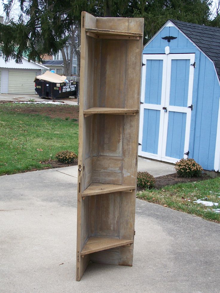 a tall wooden shelf sitting on top of a cement floor next to a blue building